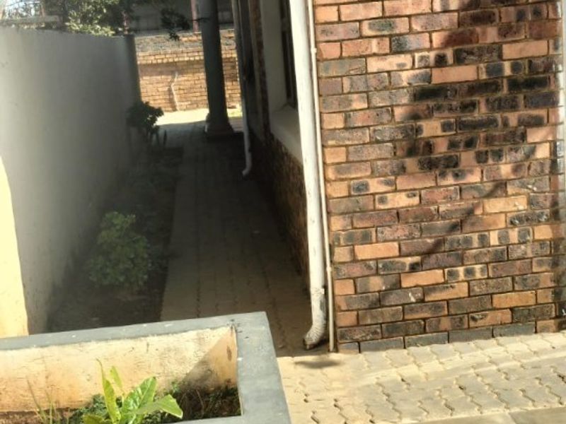 A side view of the property featuring a brick facade, paved walkway, and tiled patio area along the boundary wall.