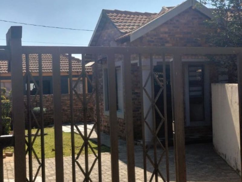 Front view of a brick-faced house featuring a paved driveway, tiled roof, and a secure metal entrance gate.