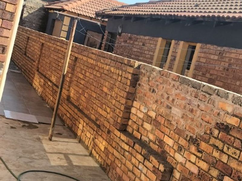 A narrow side passage featuring face brick boundary walls, concrete paving, and tiled roof structures with visible maintenance requirements.