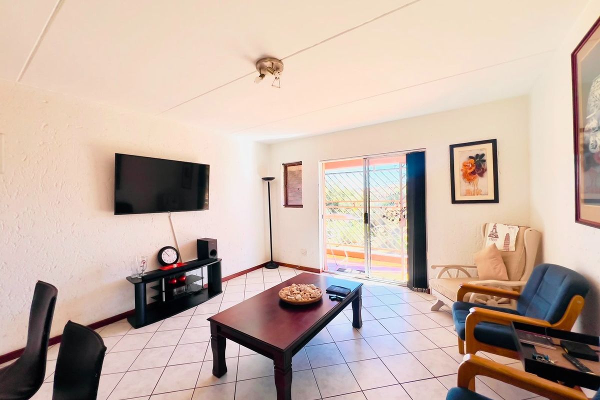 A bright living room featuring tiled flooring and a sliding glass door that provides access to an outdoor balcony area.