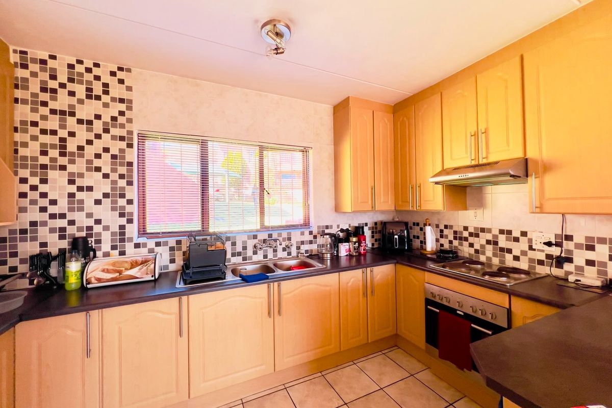 A functional kitchen featuring light wood-tone cabinetry, mosaic tile backsplash, built-in oven, electric hob, and tiled flooring with ample counter space.
