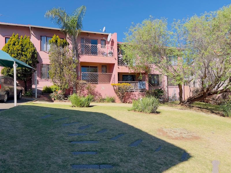 Rear view of a multi-story townhouse complex featuring private balconies, security bars, and a shared garden area with established landscaping.