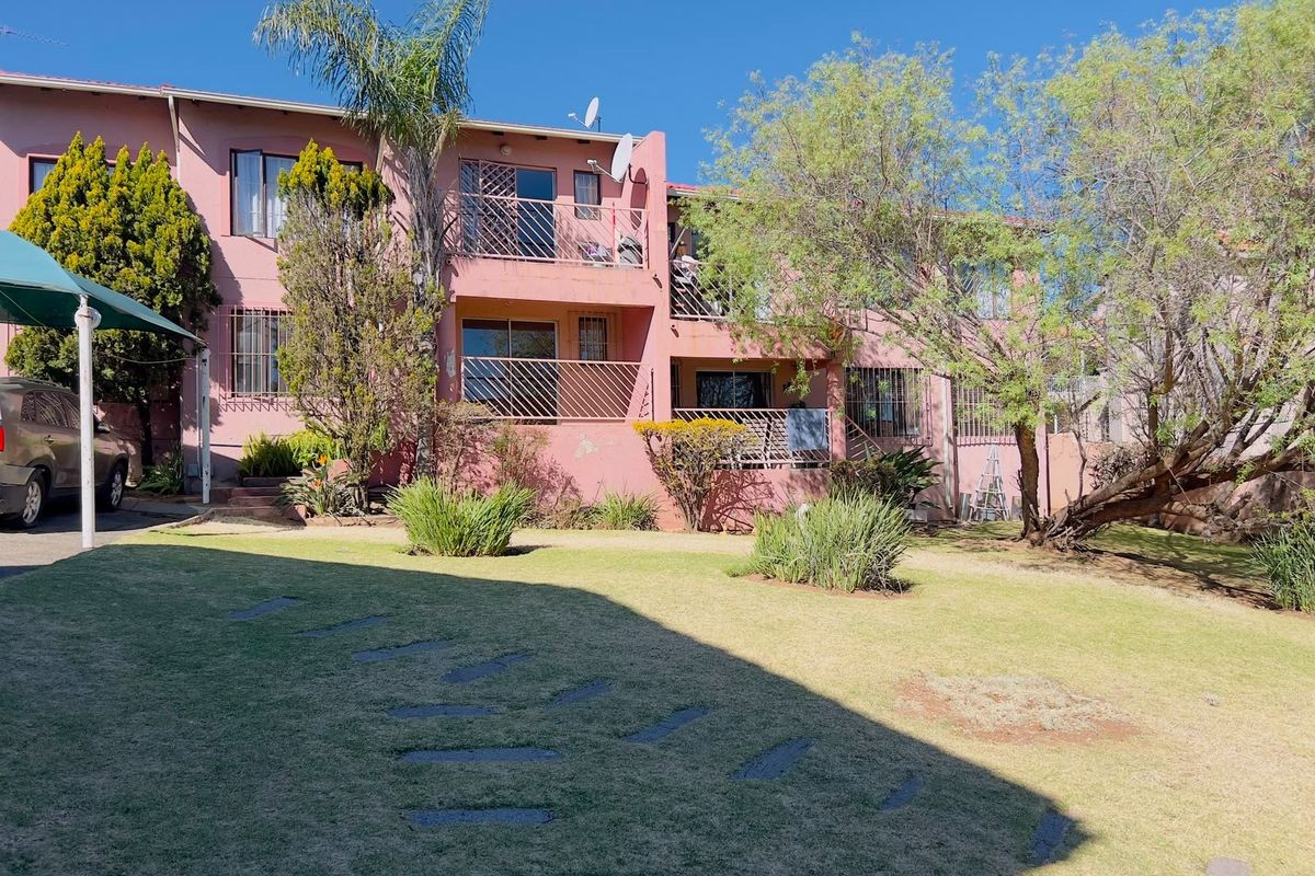 Rear view of a multi-story townhouse complex featuring private balconies, security bars, and a shared garden area with established landscaping.