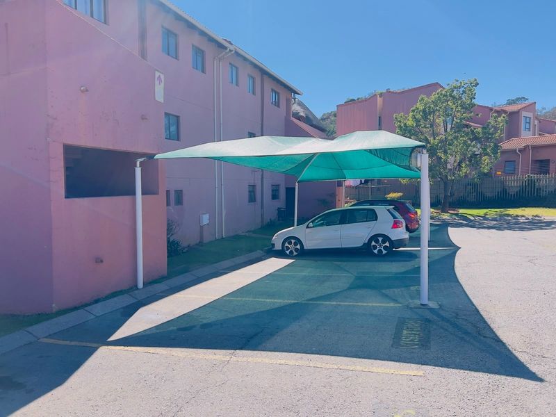 Exterior view of the townhouse complex featuring a dedicated shade cloth carport and paved parking area.