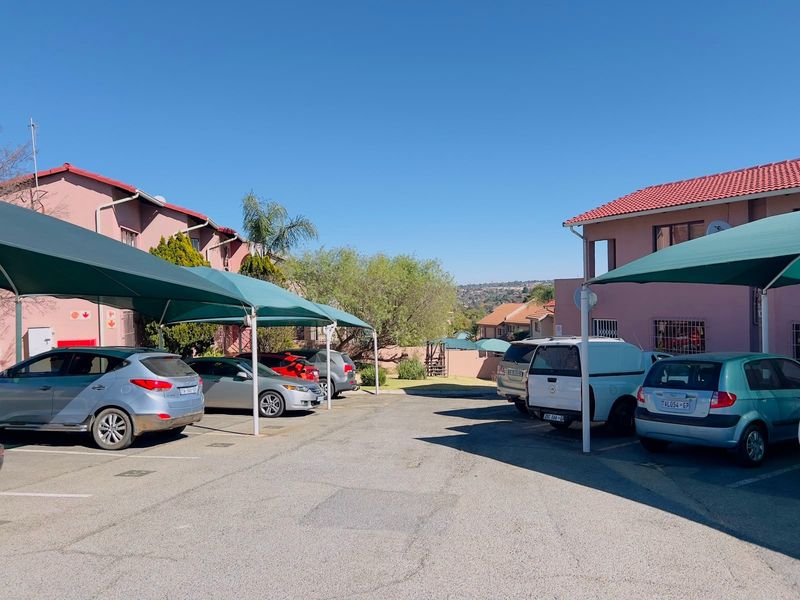 Exterior view of the townhouse complex parking area featuring shade cloth carports and paved driveway access.