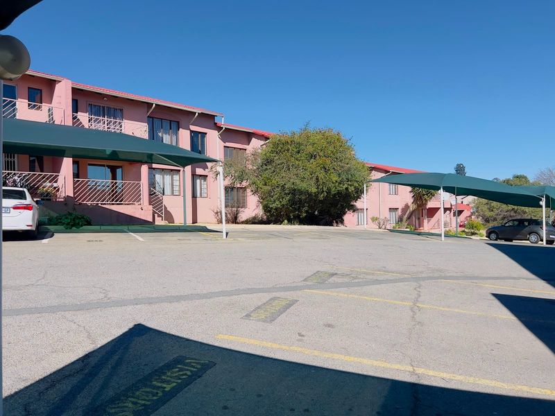 Exterior view of a townhouse complex featuring a paved parking area with shade cloth carports and multi-level residential units.