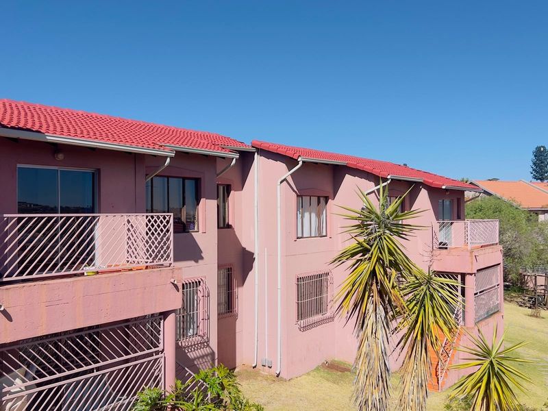 Rear elevation of a townhouse complex featuring red tiled roofing, metal security bars on windows, and private balconies with sliding door access.