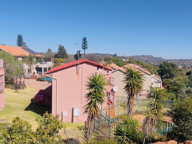 An elevated view of the rear exterior of the townhouse complex, featuring tiled roofs, communal garden space, and a swimming pool area.