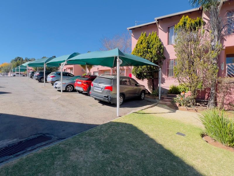 Exterior view of the townhouse complex featuring covered parking bays, paved driveway, and established garden areas with pink facade finish.