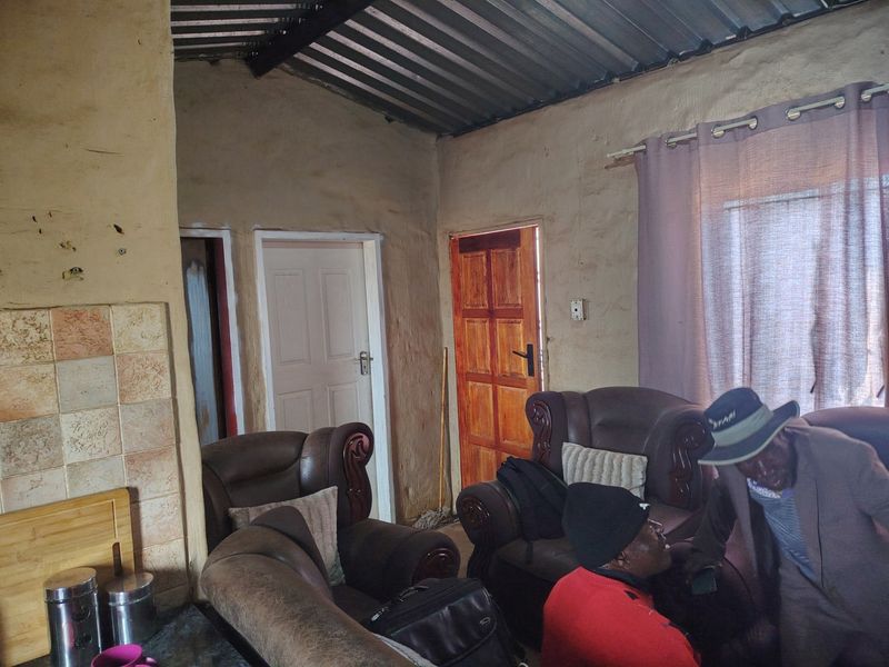 A living area featuring rustic plastered walls, a corrugated metal ceiling, and tiled accents, requiring significant cosmetic updates to improve the interior finish.