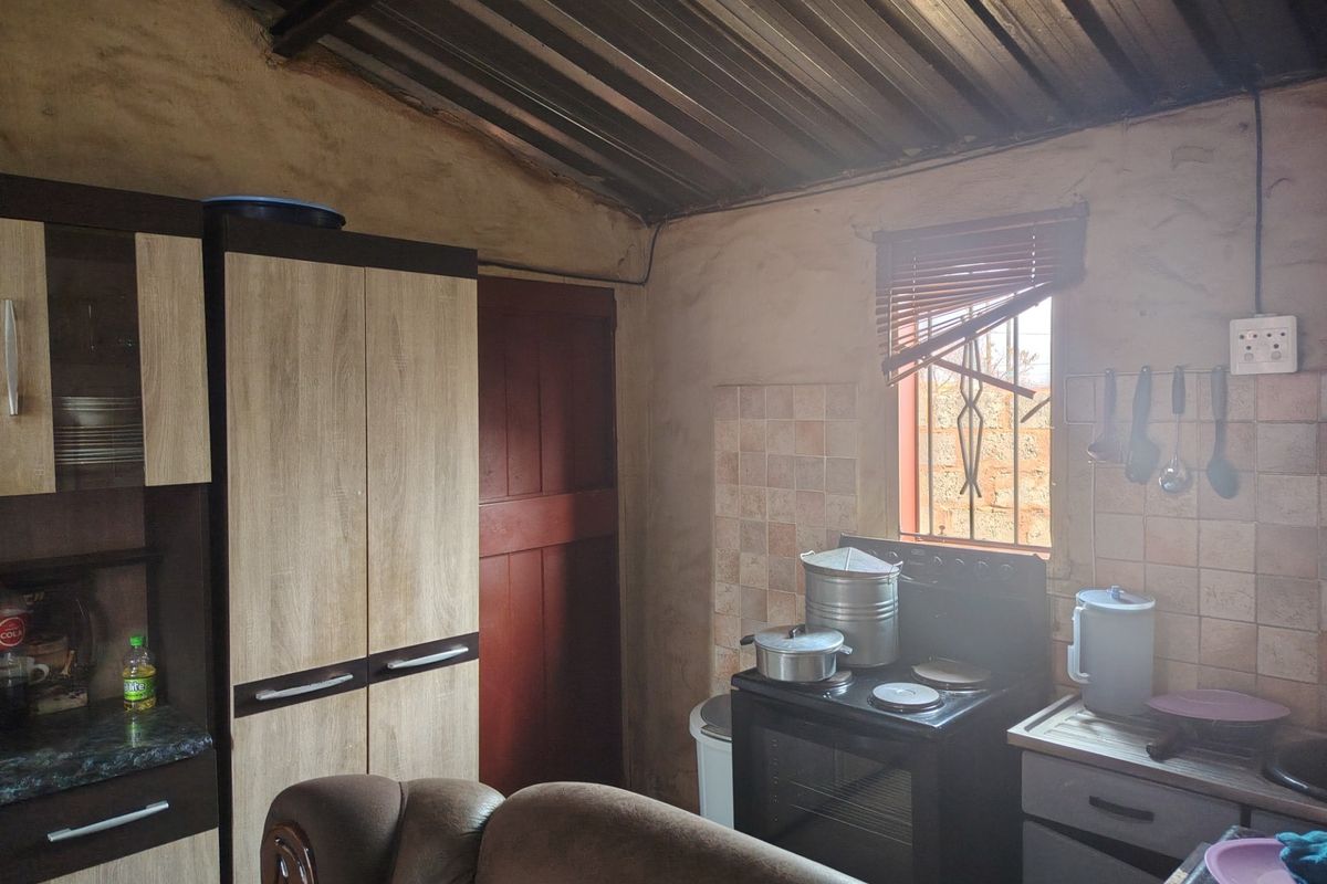 A compact kitchen featuring built-in cabinetry, a freestanding stove, and tiled splashbacks, with a rustic corrugated metal ceiling and exposed wall finishes.