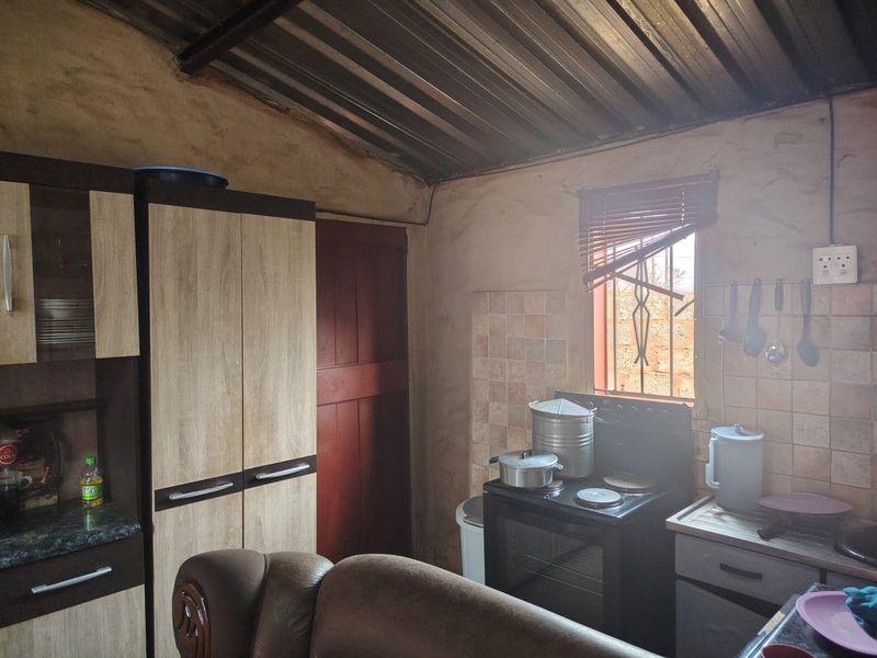 A compact kitchen featuring built-in cabinetry, a freestanding stove, and tiled splashbacks, with a rustic corrugated metal ceiling and exposed wall finishes.