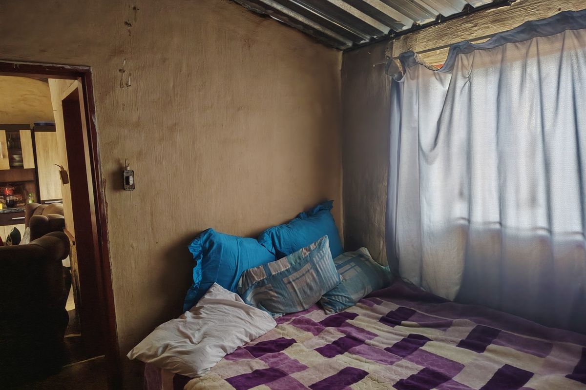A bedroom featuring plastered walls and a corrugated metal ceiling, requiring cosmetic updates to improve the overall finish and condition.