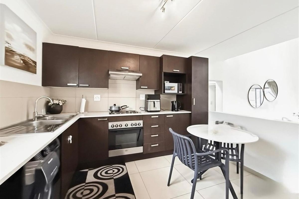 A functional kitchen featuring dark wood cabinetry, built-in oven with gas hob, extractor fan, and tiled flooring with a neutral backsplash.
