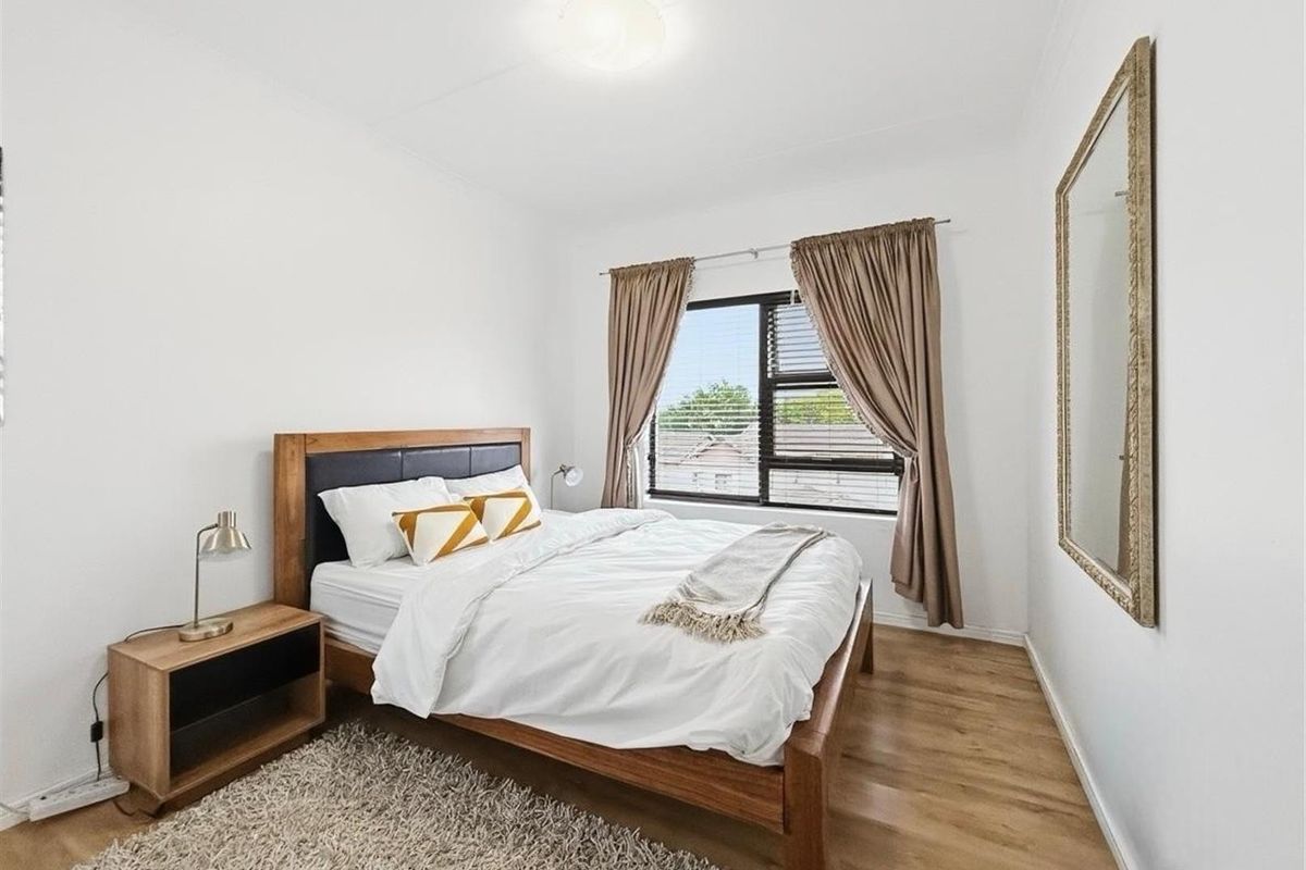 A well-maintained bedroom featuring laminate flooring, neutral white walls, and an aluminium-framed window providing natural light.