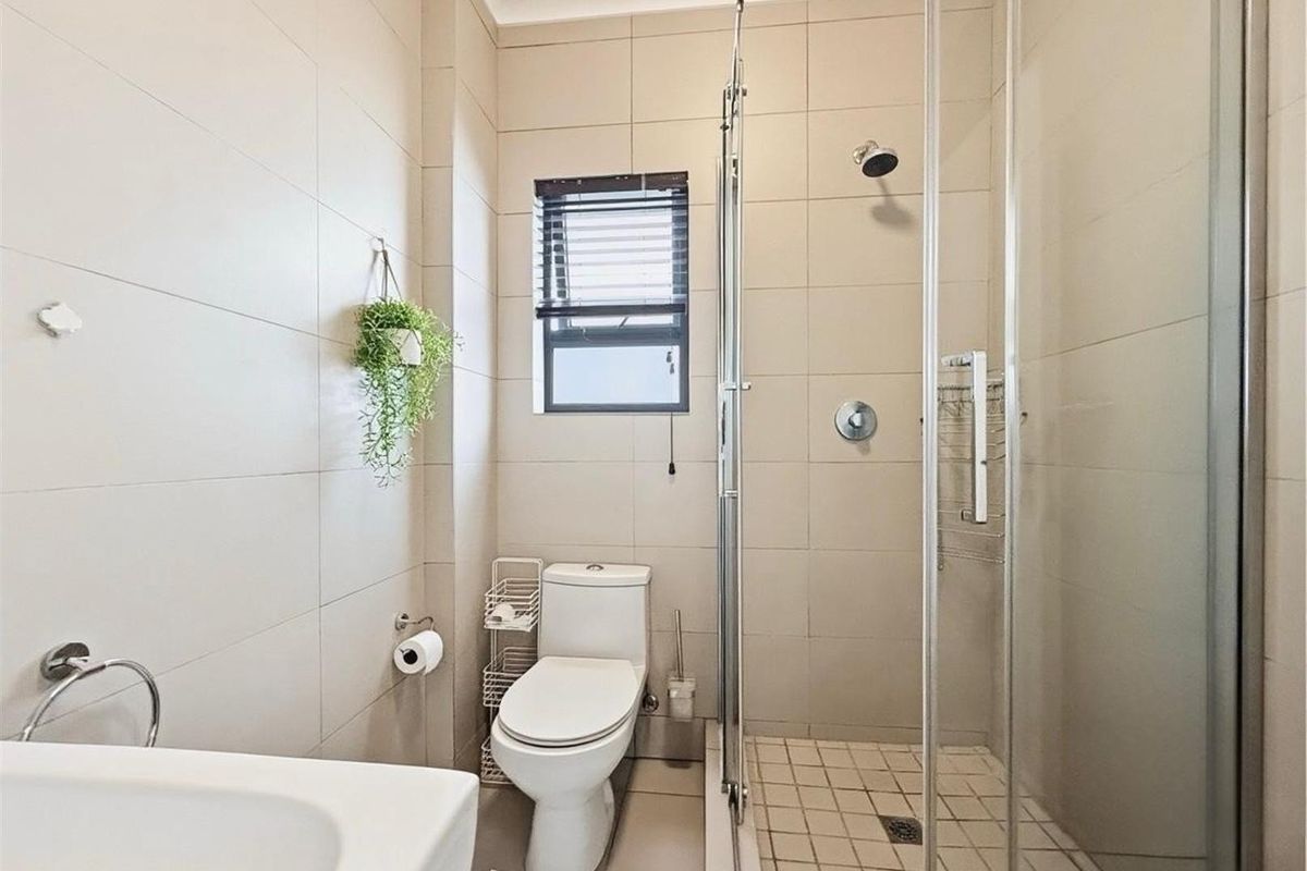 A clean and functional bathroom featuring a glass-enclosed shower, toilet, and basin with neutral wall and floor tiling.
