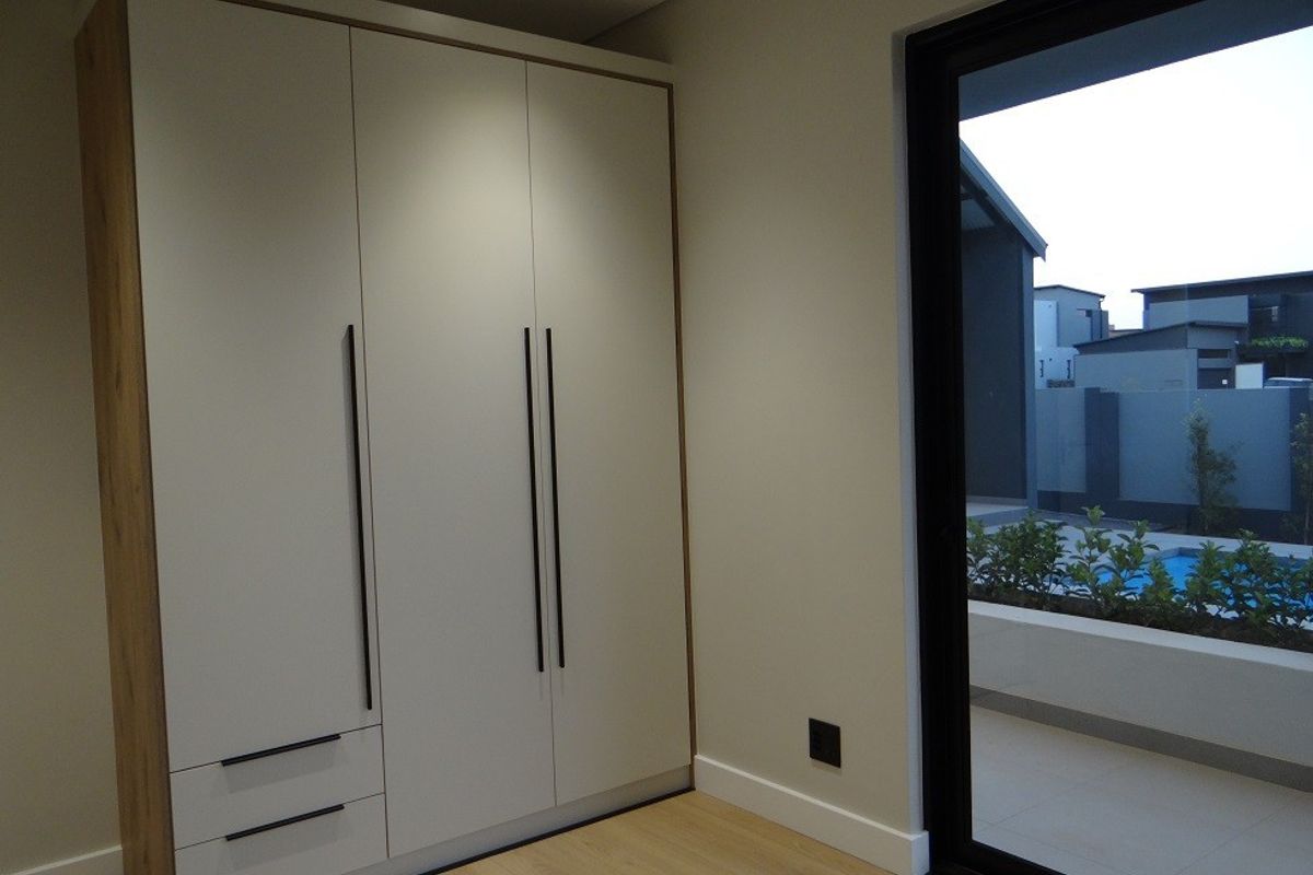 Modern bedroom featuring built-in wardrobes, light laminate flooring, and a large sliding glass door providing access to the outdoor pool area.