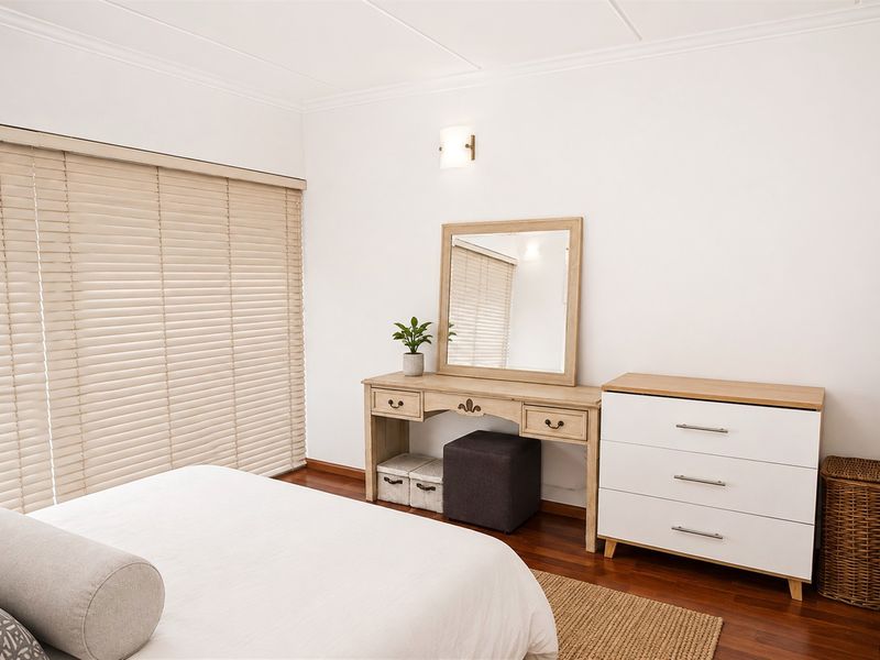 A well-maintained bedroom featuring warm hardwood flooring, neutral walls, and fitted venetian blinds, providing a clean and comfortable living space.