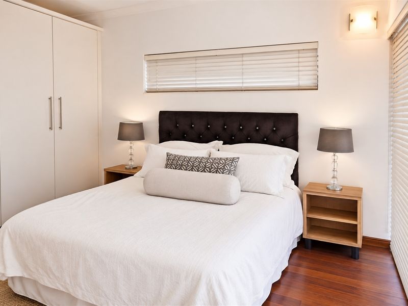 A well-maintained bedroom featuring hardwood flooring, built-in wardrobes, and venetian blinds, offering a clean and functional living space.
