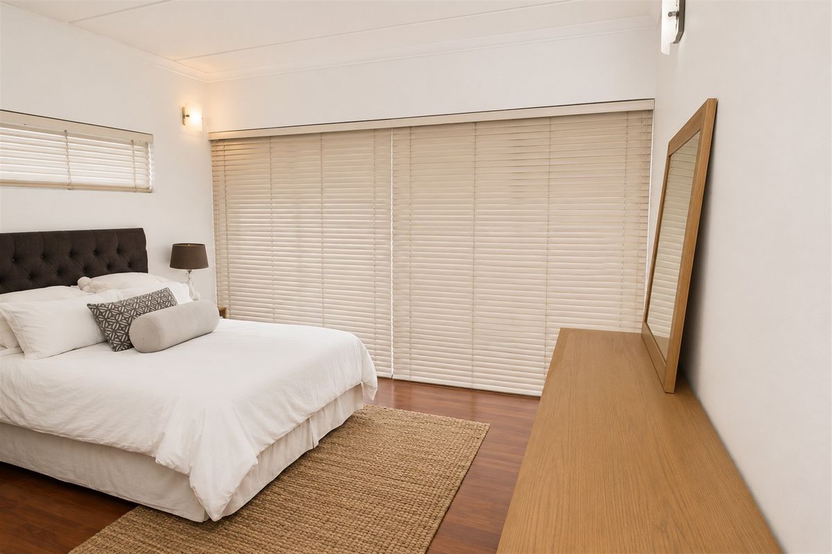 A well-maintained bedroom featuring laminate flooring, neutral wall finishes, and large venetian blinds covering the window and sliding door area.