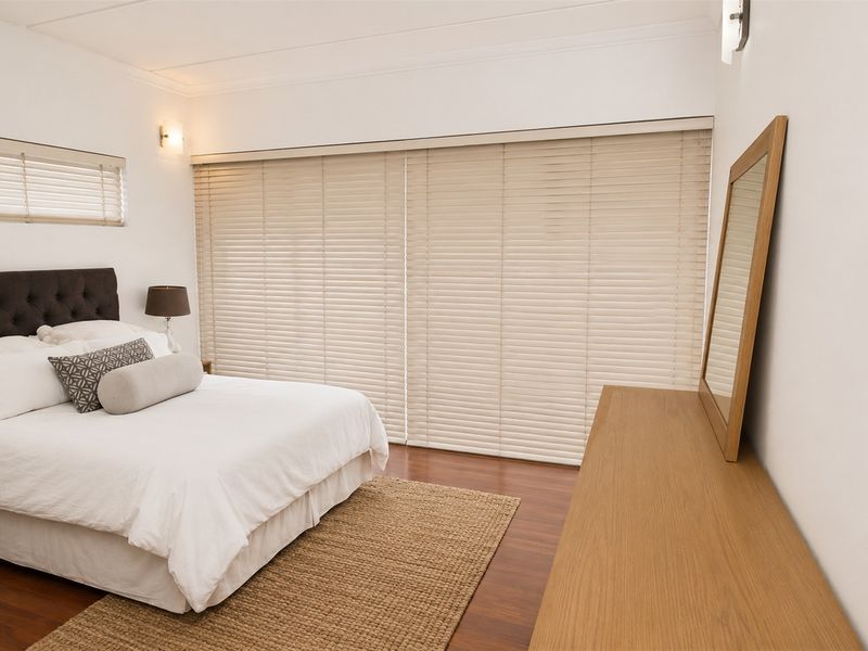 A well-maintained bedroom featuring laminate flooring, neutral wall finishes, and large venetian blinds covering the window and sliding door area.