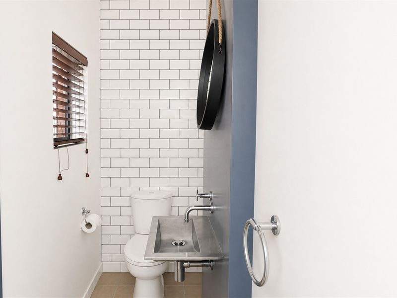 Modern guest bathroom featuring a sleek wall-mounted stainless steel basin, subway tile feature wall, and contemporary chrome fixtures.