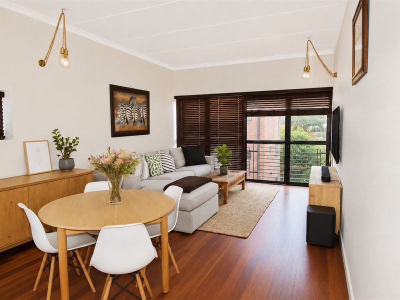 Bright open-plan living and dining area featuring warm laminate flooring, modern lighting fixtures, and large sliding doors leading to a balcony.