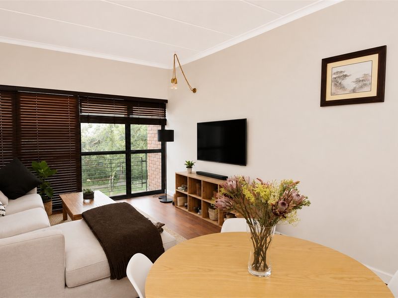 A bright open-plan living and dining area featuring laminate flooring, neutral walls, and a large sliding door with venetian blinds providing natural light.