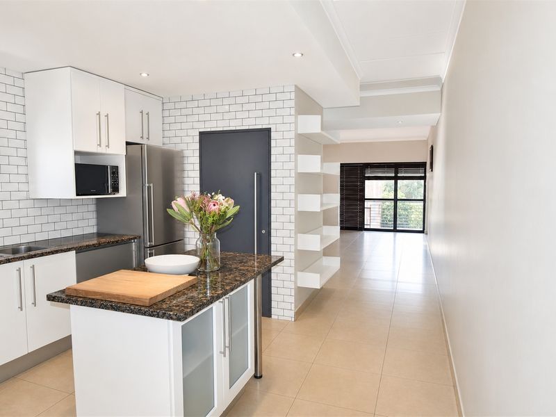 Modern open-plan kitchen featuring white cabinetry, granite countertops, a central island, and subway tile backsplash, flowing into a bright living area.