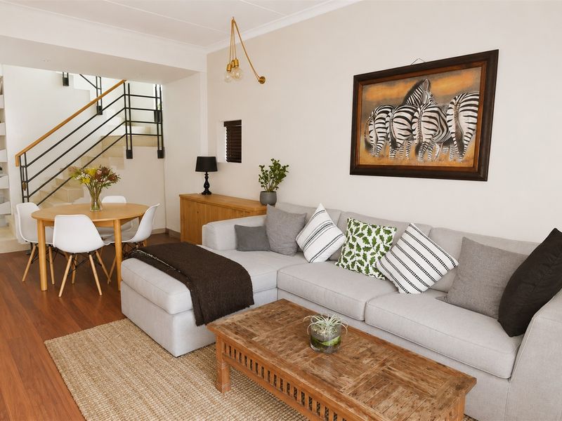 An open-plan living and dining area featuring laminate flooring, a modern staircase with metal balustrades, and neutral wall finishes.