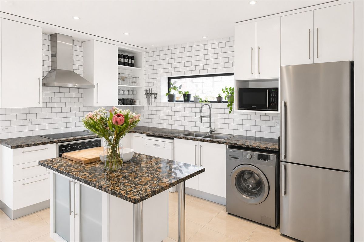 Modern kitchen featuring white cabinetry, granite countertops, subway tile backsplash, and integrated stainless steel appliances, including a central island and recessed lighting.