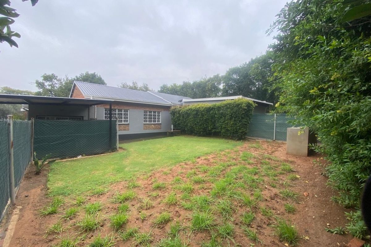 Rear view of the property featuring a lawn area, established hedging, perimeter fencing, and a covered carport structure.