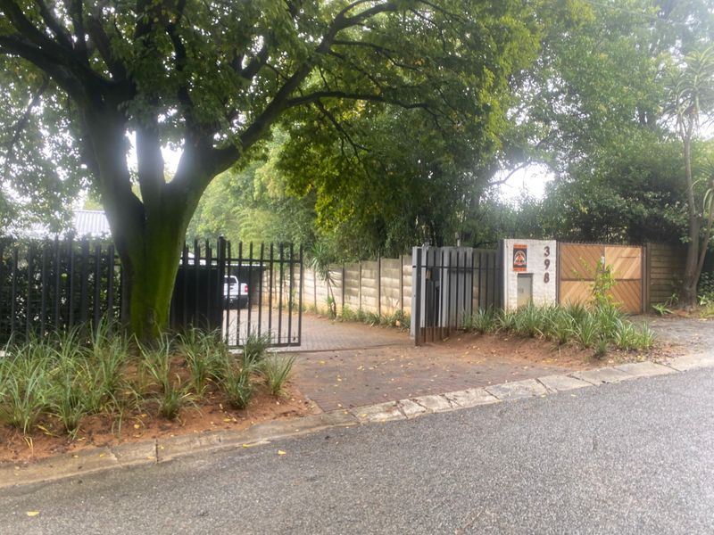 Front entrance view featuring a paved driveway, metal security gate, and established boundary wall with mature landscaping.