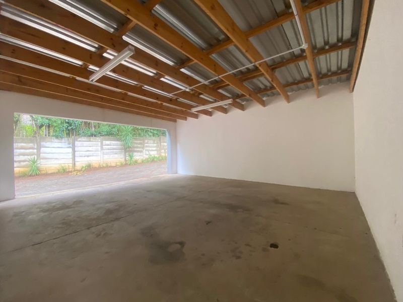 A spacious, empty garage featuring exposed timber rafters, a corrugated metal roof, and a concrete floor with direct access to the exterior.