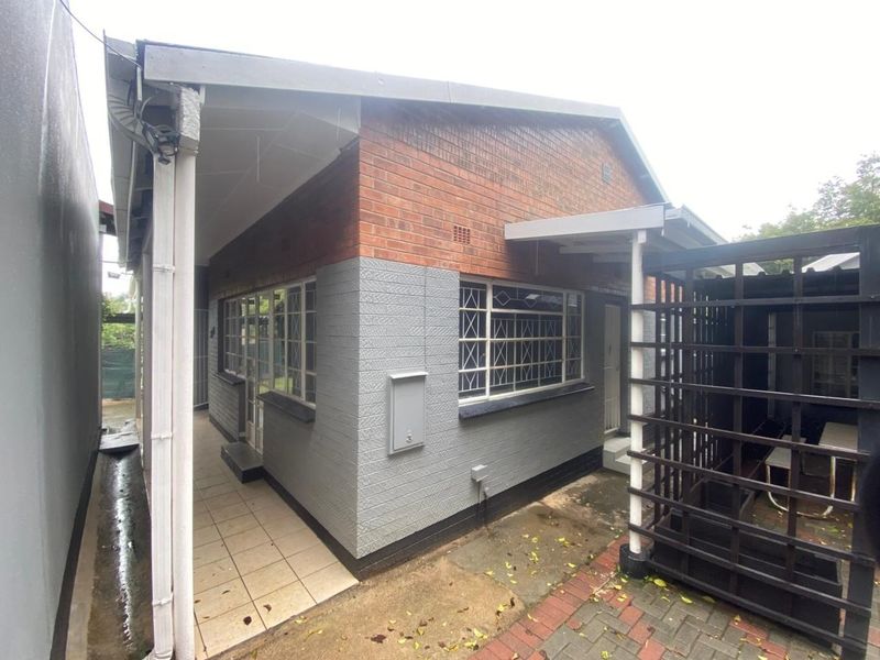 A view of the rear exterior of the house featuring a brick and painted facade, tiled patio area, and a timber trellis structure.