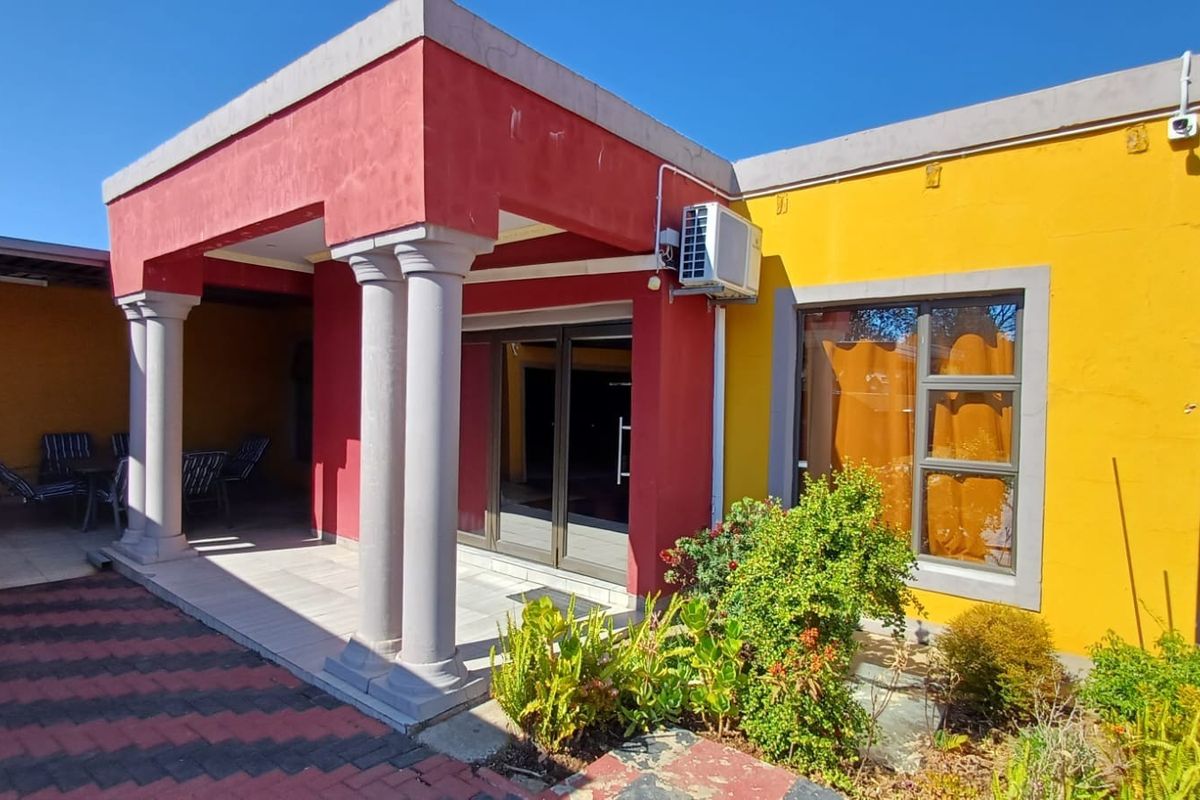 Rear exterior view of the house featuring a covered patio with concrete columns, sliding glass doors, and a paved outdoor area.