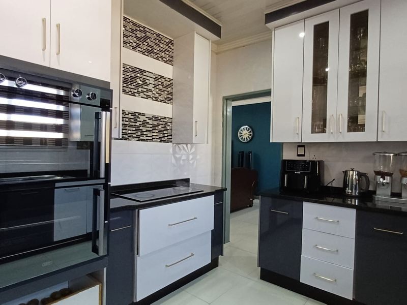 Modern kitchen featuring high-gloss cabinetry, granite countertops, built-in oven, electric hob, and stylish mosaic tile backsplash.