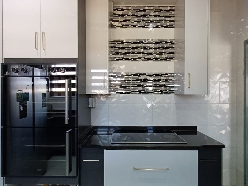 Modern kitchen featuring high-gloss cabinetry, granite countertops, a built-in oven, electric hob, and a decorative mosaic tile backsplash.