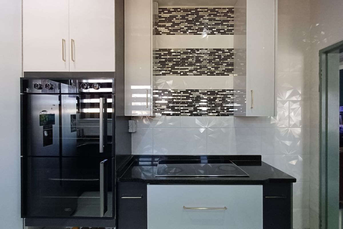 Modern kitchen featuring high-gloss cabinetry, granite countertops, a built-in oven, electric hob, and a decorative mosaic tile backsplash.