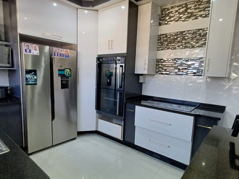 Modern kitchen featuring high-gloss cabinetry, granite countertops, built-in oven, and a decorative tiled backsplash.