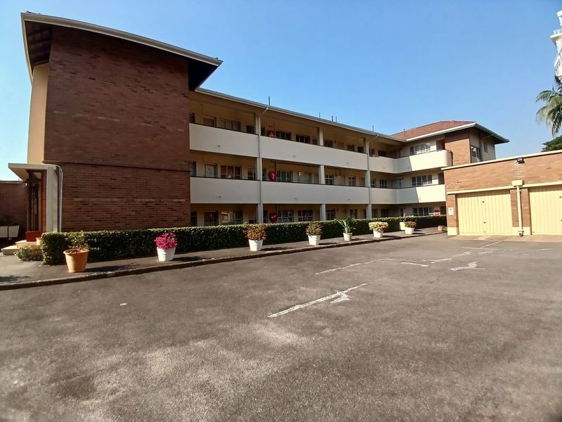 Exterior view of a multi-story apartment complex featuring a brick facade, paved driveway, and integrated garage doors.