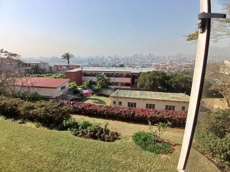 An elevated view overlooking a landscaped garden, surrounding residential properties, and the distant city skyline.
