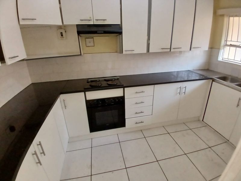 A functional kitchen featuring white cabinetry, dark countertops, built-in oven and hob, and tiled flooring, offering a clean and practical workspace.