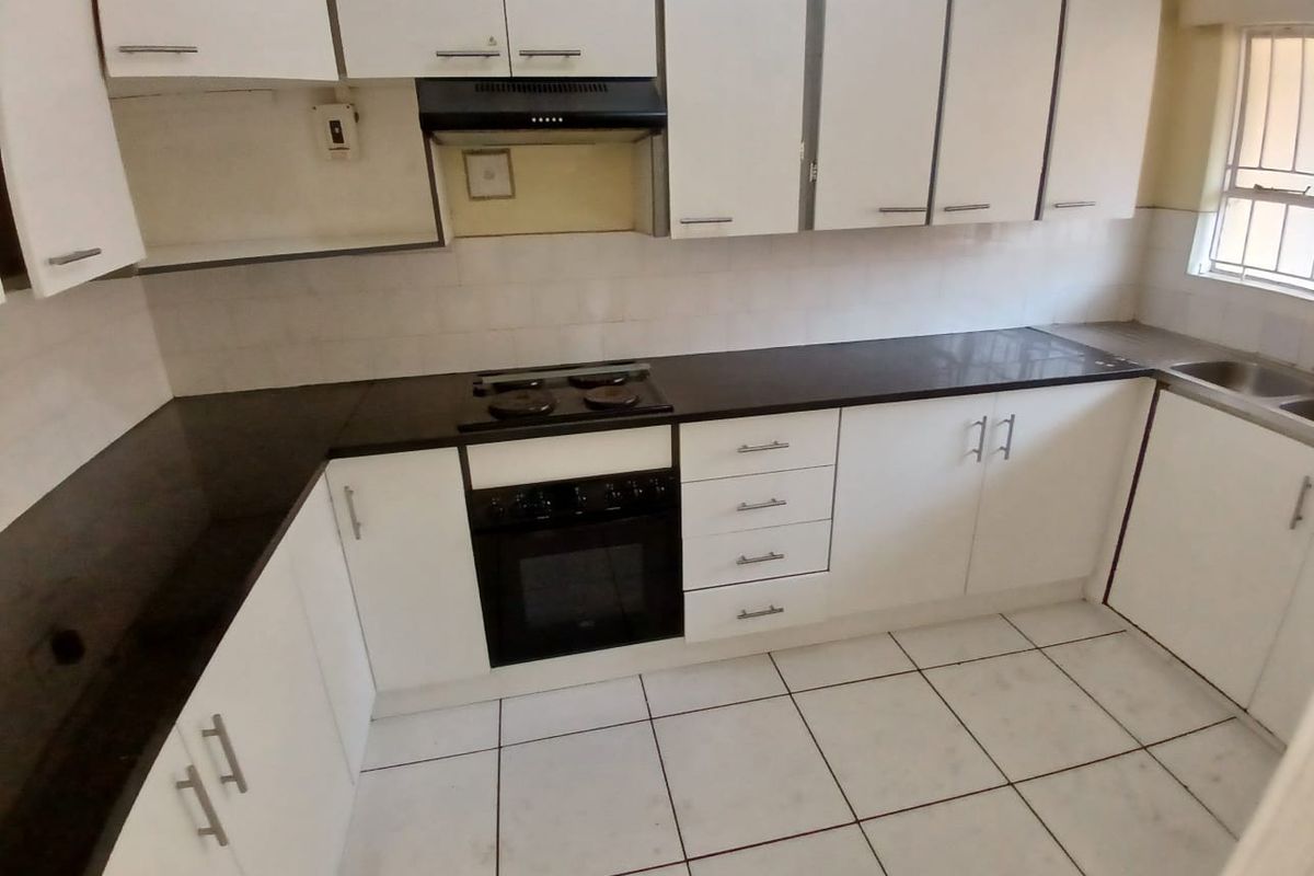 A functional kitchen featuring white cabinetry, dark countertops, built-in oven and hob, and tiled flooring, offering a clean and practical workspace.