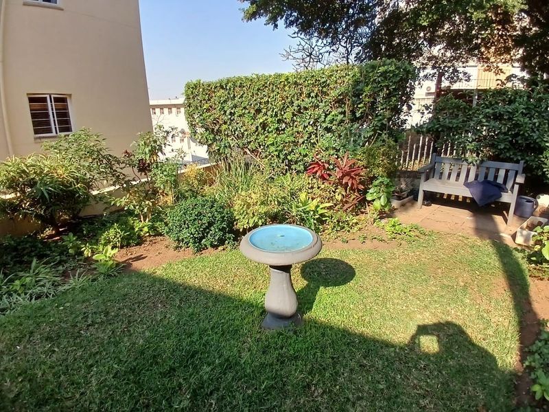 A well-maintained private garden area featuring established hedging, lawn, and paved sections, providing a pleasant outdoor space for the apartment.