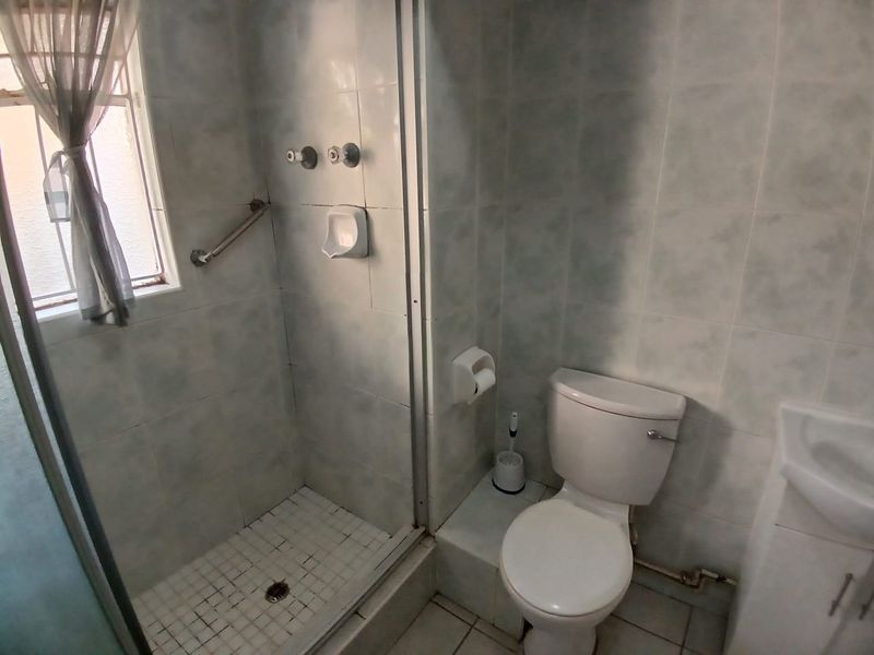 Compact bathroom featuring a shower enclosure, toilet, and vanity basin with dated wall tiling and functional fixtures.