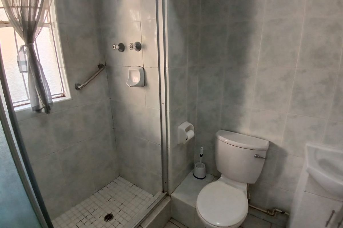 Compact bathroom featuring a shower enclosure, toilet, and vanity basin with dated wall tiling and functional fixtures.