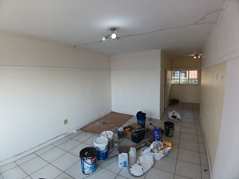An empty living area featuring ceramic floor tiles and a ceiling light fixture, currently undergoing maintenance with visible ceiling cracks.