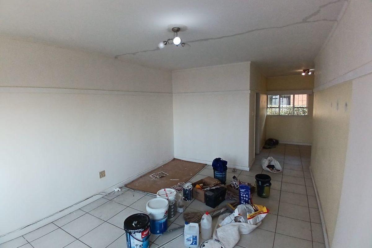 An empty living area featuring ceramic floor tiles and a ceiling light fixture, currently undergoing maintenance with visible ceiling cracks.