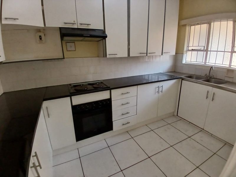 A functional kitchen featuring white cabinetry, dark countertops, an integrated oven and hob, and tiled flooring with a window providing natural light.